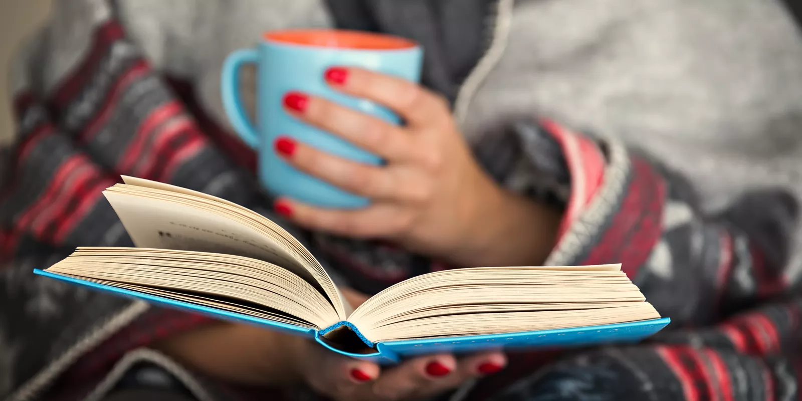 person wrapped in a cozy blanket with a book and cup of coffee