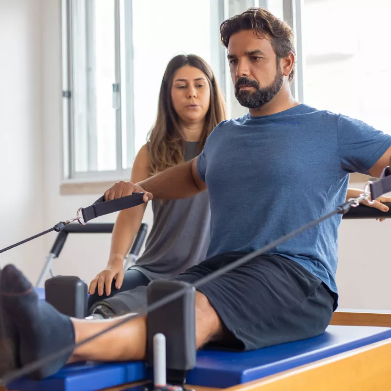 Pilates instructor helping a patient use the reformer equipment